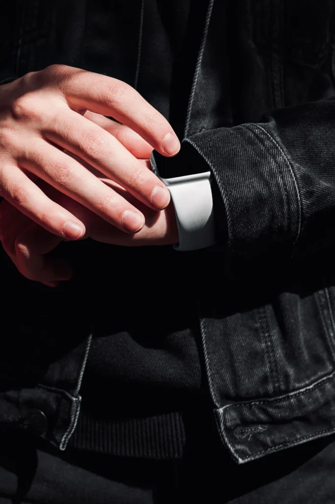 Hand in schwarzem Denimärmel mit Smartwatch, Detailaufnahme der Ärmelöffnung und Knopfleiste