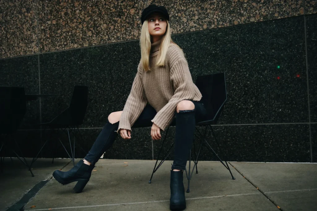 Frau mit schwarzen Stiefeletten, schwarzer Jeans und beigem Strickpullover im herbstlichen Streetstyle