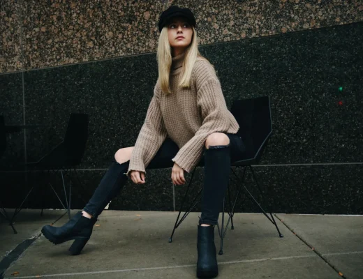 Frau mit schwarzen Stiefeletten, schwarzer Jeans und beigem Strickpullover im herbstlichen Streetstyle