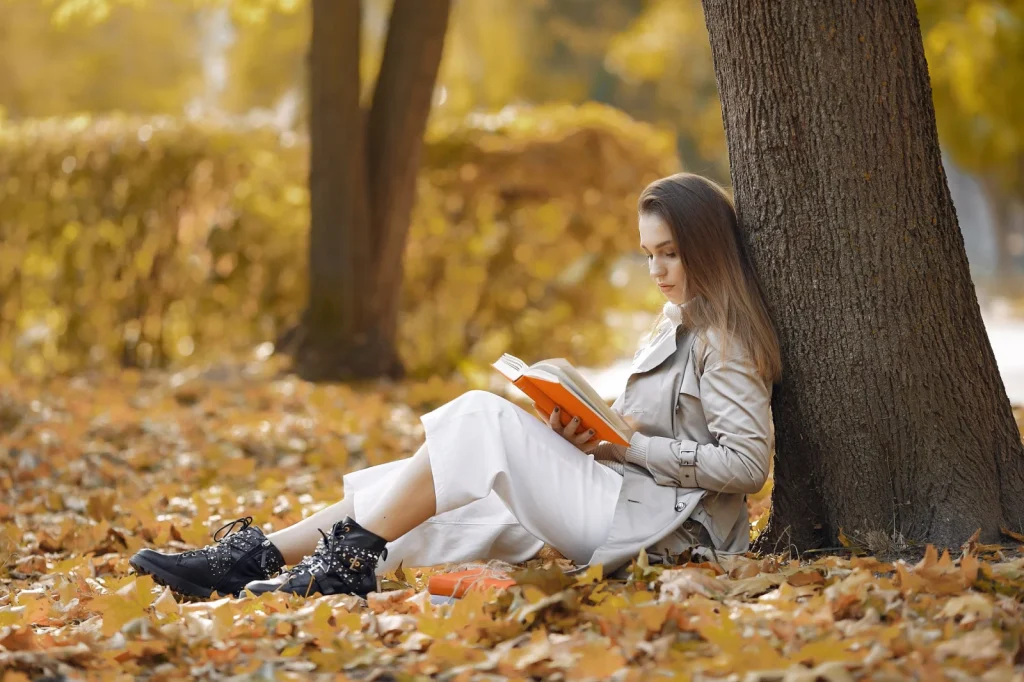 Frau liest im Herbst ein Buch unter einem Baum im Park