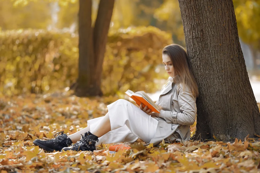 Frau liest im Herbst ein Buch unter einem Baum im Park