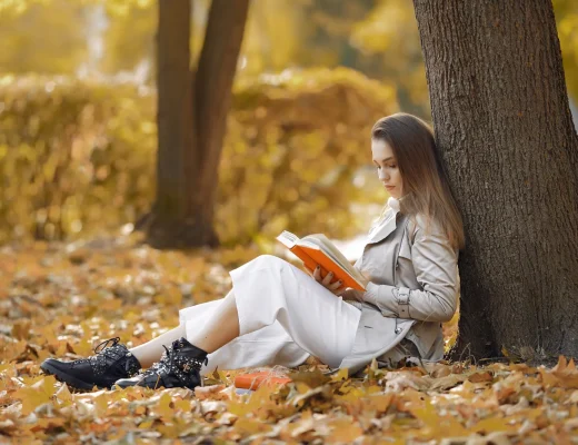 Frau liest im Herbst ein Buch unter einem Baum im Park