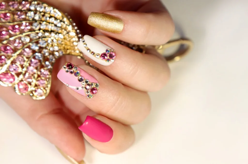 Bunte Gem Nails mit rosa, weißen und goldenen Nägeln, verziert mit funkelnden Strasssteinen im 90er-Stil.