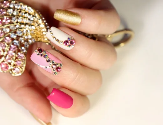 Bunte Gem Nails mit rosa, weißen und goldenen Nägeln, verziert mit funkelnden Strasssteinen im 90er-Stil.