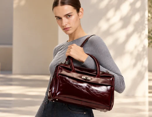 Model mit glänzender bordeauxfarbener Liebeskind Archive Gloria II Handtasche, grauem Rippoberteil und dunkler Jeans.