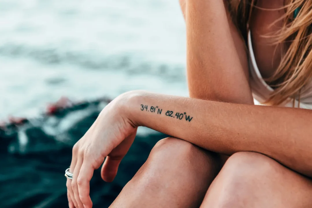 Frau mit einem kleinen Koordinaten-Tattoo am Unterarm