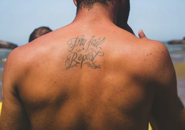 Mann mit älterem Schriftzug-Tattoo auf dem oberen Rücken