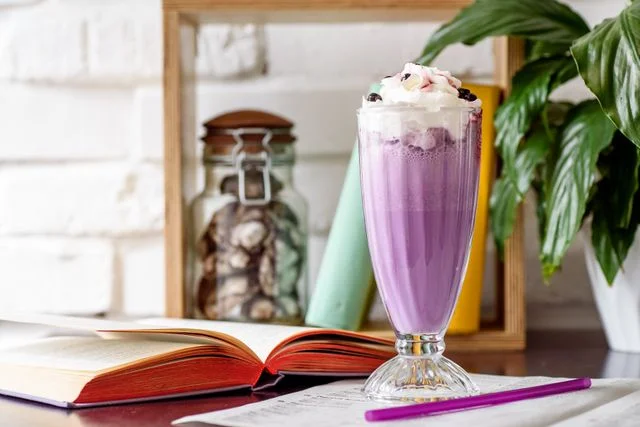 Violetter Milchshake mit Sahnehaube in einem hohen Glas auf einem Tisch