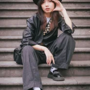 Junge Frau im modernen Korean-Style mit schwarzem Hut und Oversized-Look auf einer Treppe