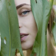 Frau mit strahlender Haut blickt durch grüne Blätter – natürliche Schönheit und frischer Glow