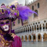Maskierte Gestalt in violett-goldenen Kostümen vor dem Dogenpalast – künstlerisches Symbol für die Filmfestspiele Venedig 2025.