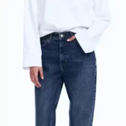 Frau trägt dunkelblaue Mom Jeans mit hohem Bund, kombiniert mit weißem Oversize-Pullover und schwarzen Ballerinas – minimalistischer Herbstlook 2025.