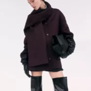Mantel Damen bordeaux – kurzer Wollmantel mit Oversize-Schal, schwarze Lederhandschuhe und Overknee-Stiefel zu Minirock/Shorts vor hellem Hintergrund.