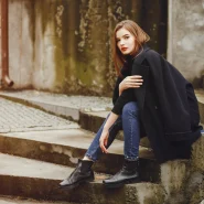 Frau im dunkelblauen Mantel und Skinny-Jeans trägt schwarze Chelsea Boots und sitzt auf Treppen im urbanen Herbst-Setting