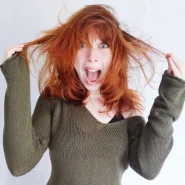 Frau mit roten, verfilzten Haaren zieht frustriert an zwei Strähnen – SOS-Moment beim Entwirren, Thema „verfilzte Haare lösen“