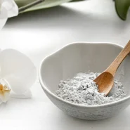 Kollagen Pulver in einer grauen Keramikschale mit Holzlöffel neben einer weißen Orchideenblüte – minimalistisches Beauty-Stillleben für Hautpflege und Anti-Aging.