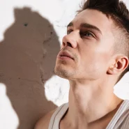 Symbolbild Low Fade: junger Mann mit sauber verblendetem Fade-Haarschnitt, Seiten kurz, Blick nach oben an einer Betonwand