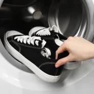 Sneaker waschen: schwarze Canvas-Sneaker werden in eine Waschmaschine gelegt, Nahaufnahme einer Hand an der Ferse