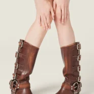 Kniehohe, braune Lederstiefel mit seitlichen Schnallen und Blockabsatz, gestylt zum kurzen Wollrock.