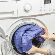 Daunenjacke waschen: blaue Steppjacke wird in eine Frontlader-Waschmaschine gelegt