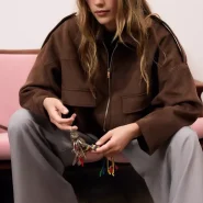 Eine Frau sitzt auf einem rosa Sofa und hält ein braunes Accessoire in der Hand