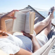 Eine Frau liegt in einer Hängematte am Strand und liest ein Buch