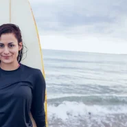Dame im schwarzen Rashguard mit Surfbrett am Strand
