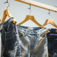 Verschiedene Jeans in verschiedenen Blautönen hängen auf Holzkleiderbügeln an einer Stange