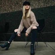 Frau mit schwarzen Stiefeletten, schwarzer Jeans und beigem Strickpullover im herbstlichen Streetstyle